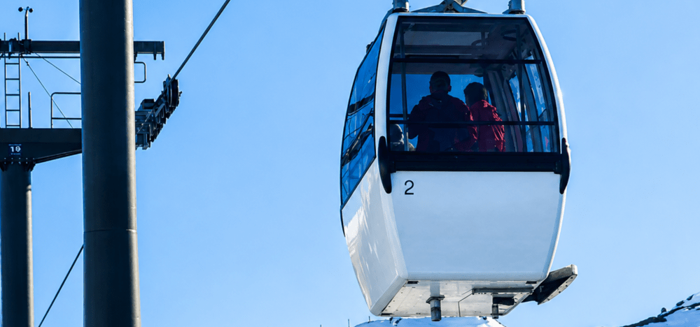 Two people in a ski gondola against a clear blue sky.
