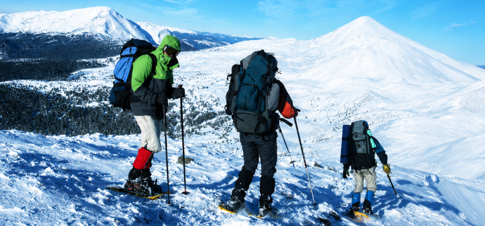 Three hikers in snow gear with backpacks and poles on a snowy mountain slope.