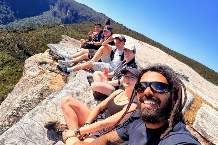 Group of people seated on a cliff edge with a scenic view.