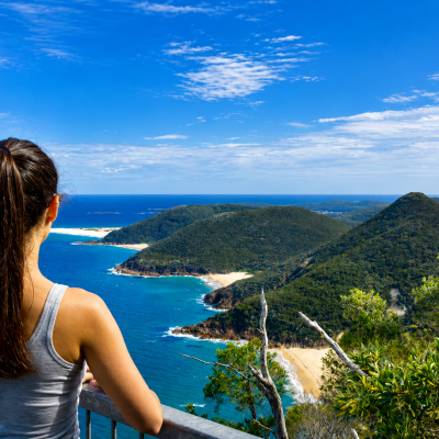 Woman overlooking a coastal view with blue ocean and green hills.