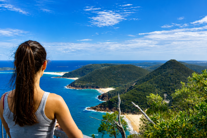 Woman overlooking a coastal view with blue ocean and green hills.