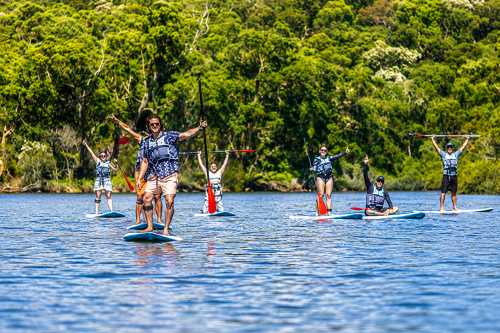 Group paddleboarding on a lake with lush green trees in the background.