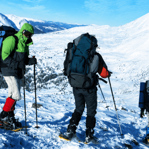 Three hikers in snow gear with backpacks and poles on a snowy mountain slope.
