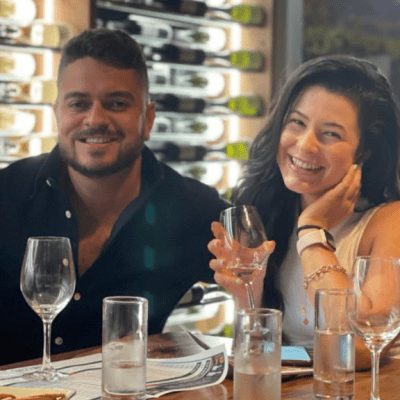 Two people smiling at a table with wine glasses and a wine rack in the background.