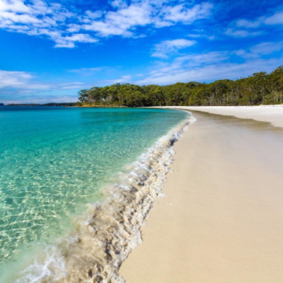 Pristine beach with turquoise water, white sand, and a forested background under a blue sky with clouds.