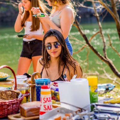 Woman in sunglasses at outdoor picnic with food and friends.