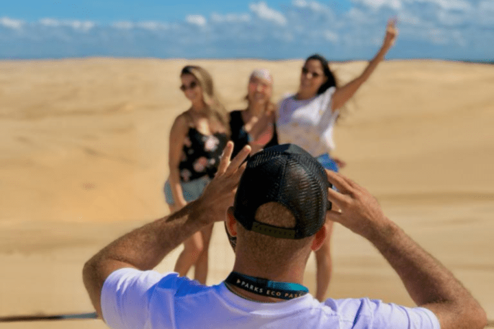 Person taking photo of three people posing in a desert landscape.