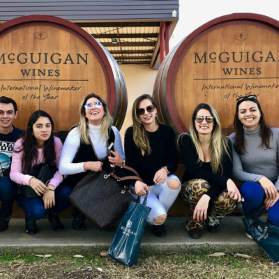 Group of seven people sitting by large wine barrels outside McGuigan Wines.