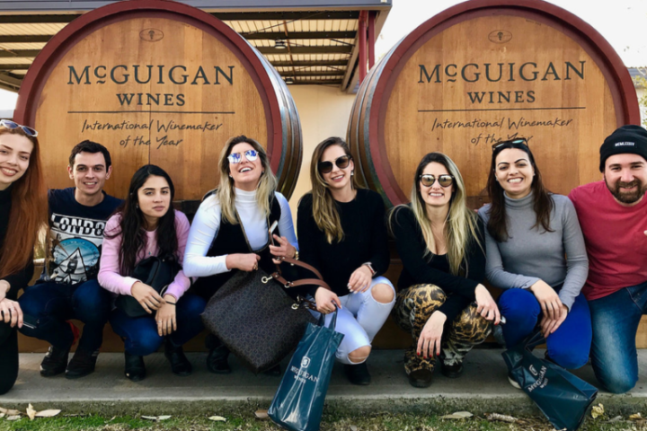 Group of seven people sitting by large wine barrels outside McGuigan Wines.