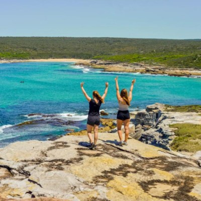 Two people celebrating on a rocky cliff above a turquoise ocean.