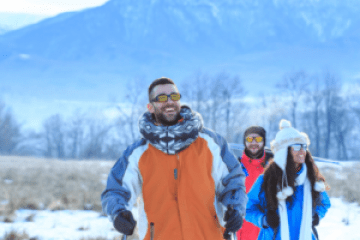Group of three people walking in snowy landscape with mountains.