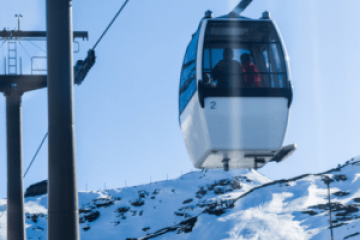 Ski lift gondola on snowy mountain under blue sky.