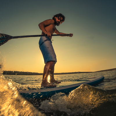 Man paddleboarding on lake at sunset with water splash.