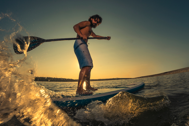 Man paddleboarding on lake at sunset with water splash.