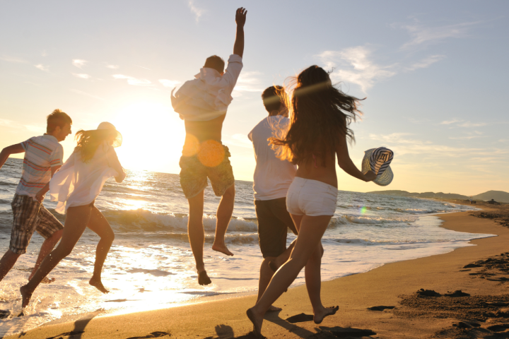 Group of people joyfully running on the beach at sunset.