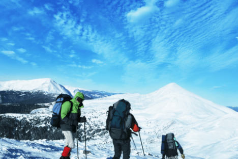 Three mountaineers trekking on snowy mountain under blue sky.