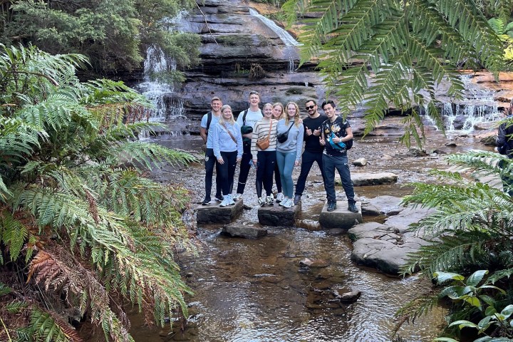 Group of people posing by a waterfall surrounded by lush greenery.