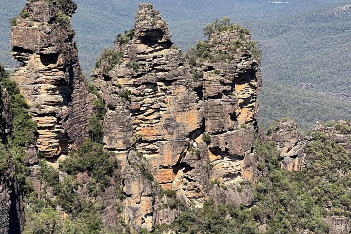 Rock formation with green vegetation, mountains in the background.