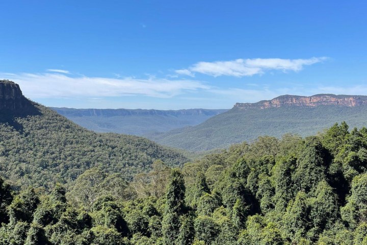 Lush green valley with distant mountains and clear blue sky.