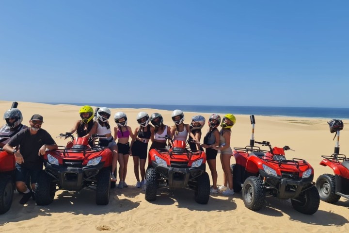 Group wearing helmets on red ATVs in sandy desert landscape.