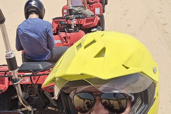 Group of people riding red ATVs in a desert, wearing helmets.