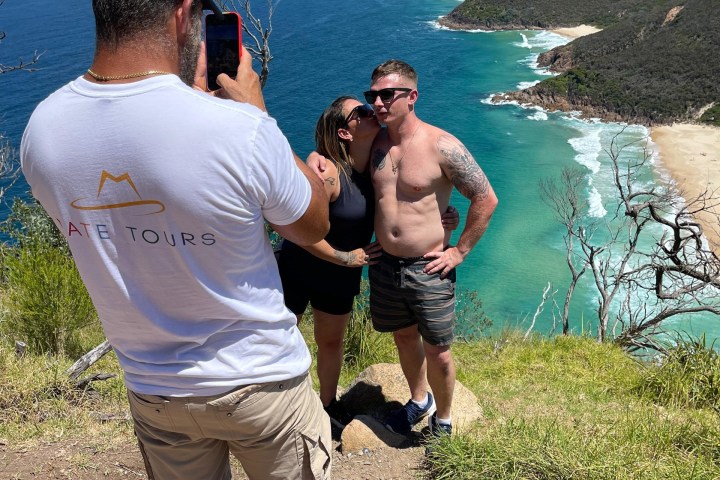 Couple posing for photo on cliff with ocean and beach view.