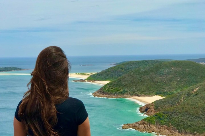 Person with long hair overlooks ocean and coastline from a high vantage point.